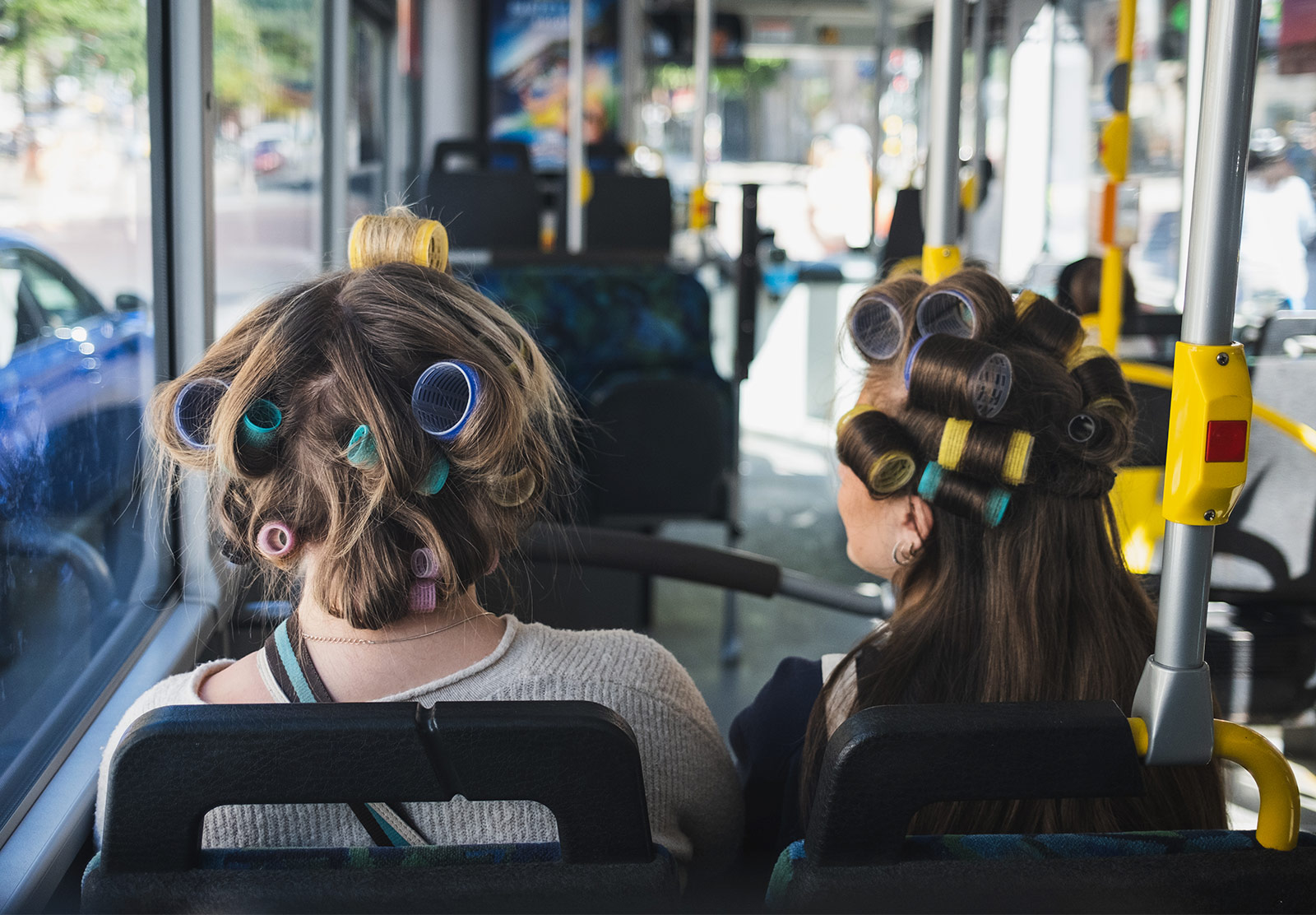 Two girls sat on bus with rollers in their hair